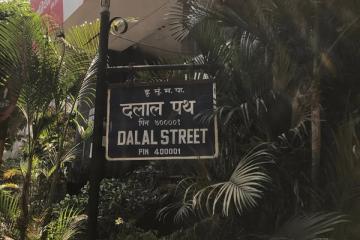 Blue Dalal Street sign in Hindi and English, with palm trees behind it.