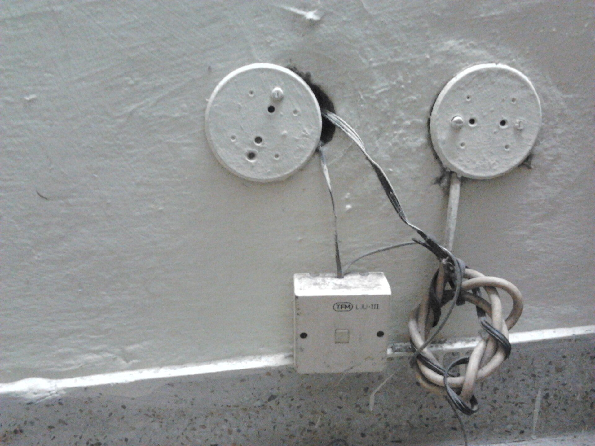 Telephone junction box on a painted wall with two round cover plates and loose cables coiled beneath
