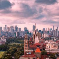Mumbai skyline of high-rise towers, a clock tower and green parkland under a cloudy sky