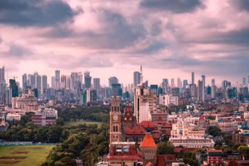 Mumbai skyline of high-rise towers, a clock tower and green parkland under a cloudy sky