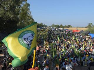 Large crowd of farmers seated along a road with green and yellow union flags, tents and trees in the background