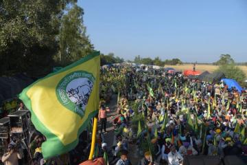 Large crowd of farmers seated along a road with green and yellow union flags, tents and trees in the background