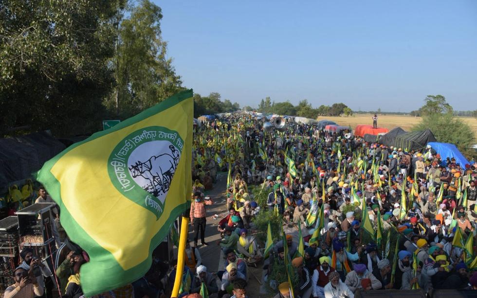 Large crowd of farmers seated along a road with green and yellow union flags, tents and trees in the background