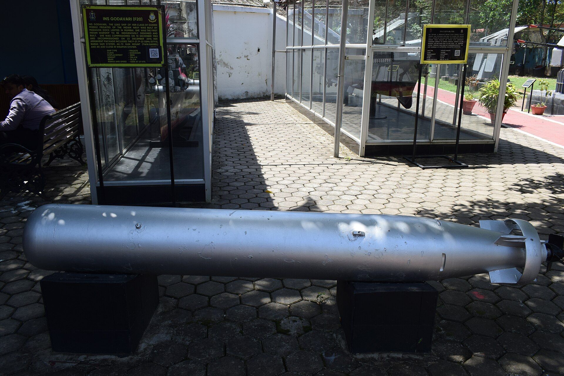 Silver torpedo lying on a paved outdoor area in front of glass display cases and information boards