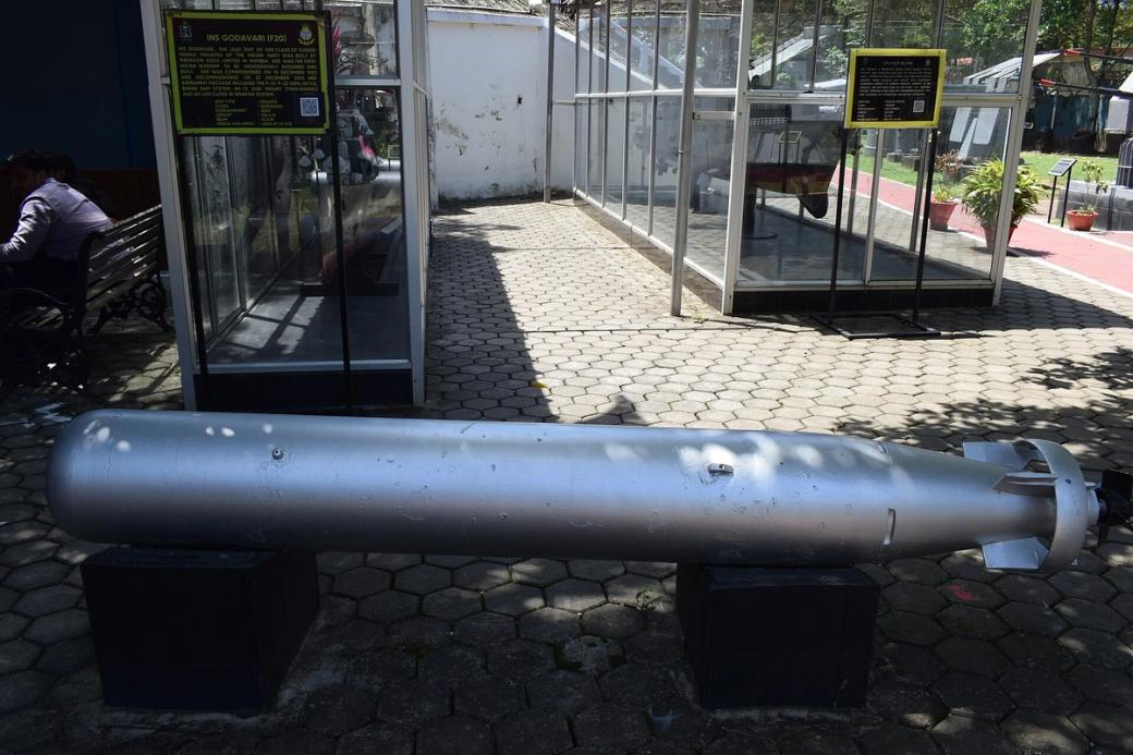 Silver torpedo lying on a paved outdoor area in front of glass display cases and information boards