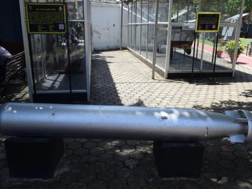 Silver torpedo lying on a paved outdoor area in front of glass display cases and information boards