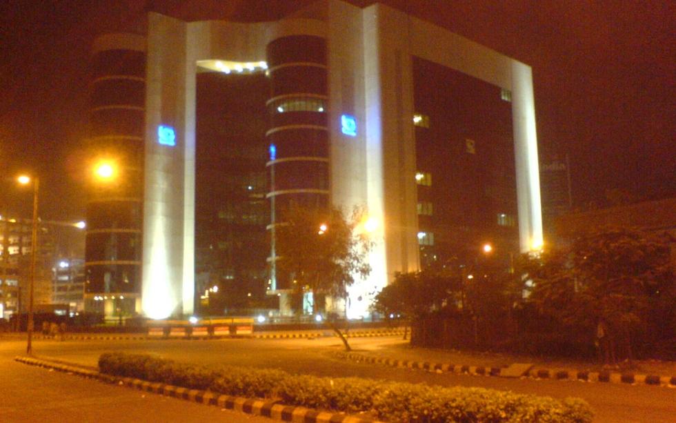 Night view of the SEBI building in Bandra Kurla Complex, its arched concrete frame lit against a dark sky.