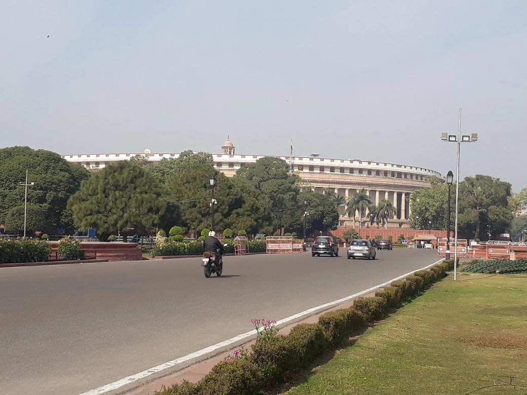 Motorcycle and cars on a wide road with lawns and a domed government building in the background, New Delhi