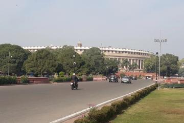 Motorcycle and cars on a wide road with lawns and a domed government building in the background, New Delhi