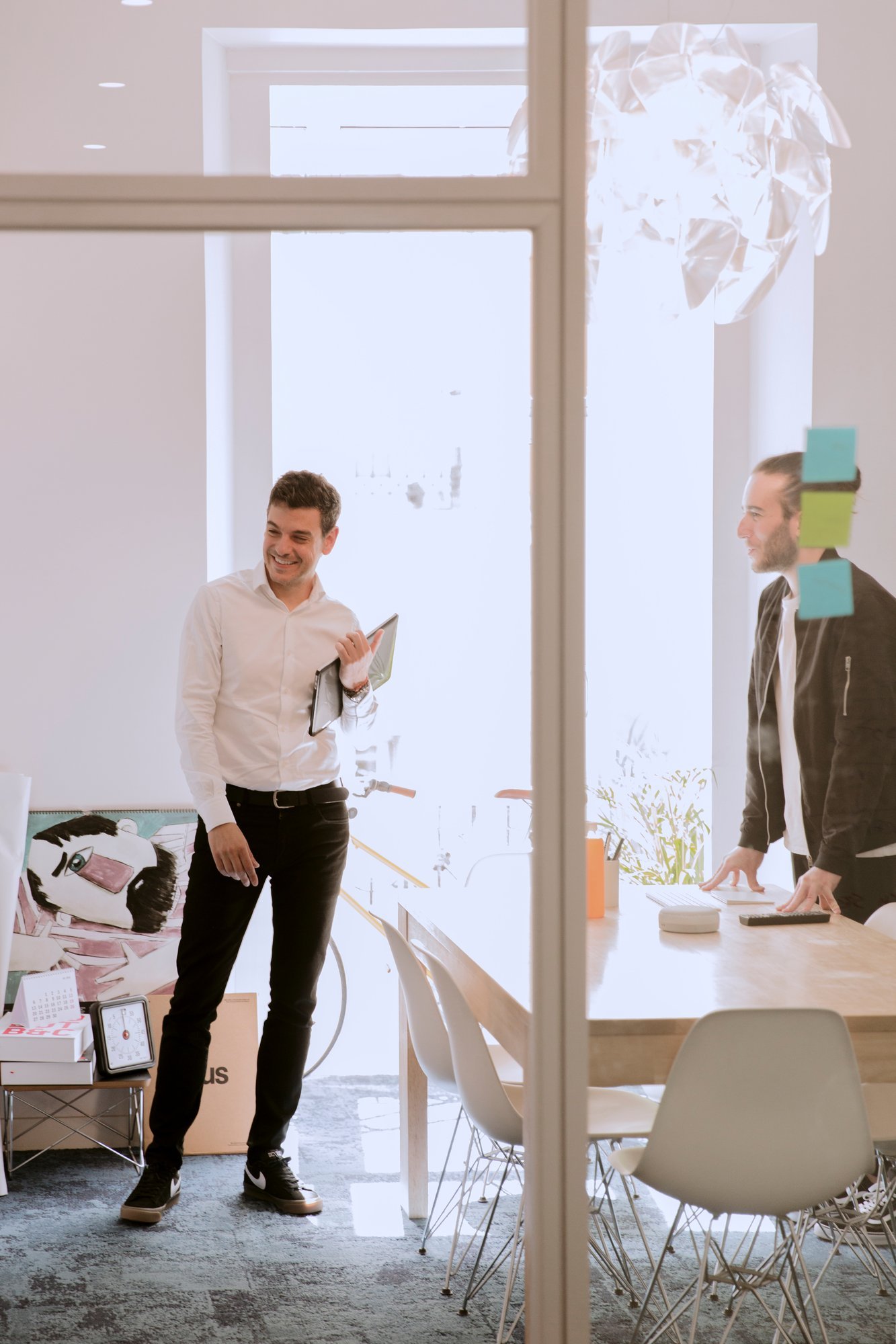 Dos compañeros conversando de pie en una sala de reuniones luminosa