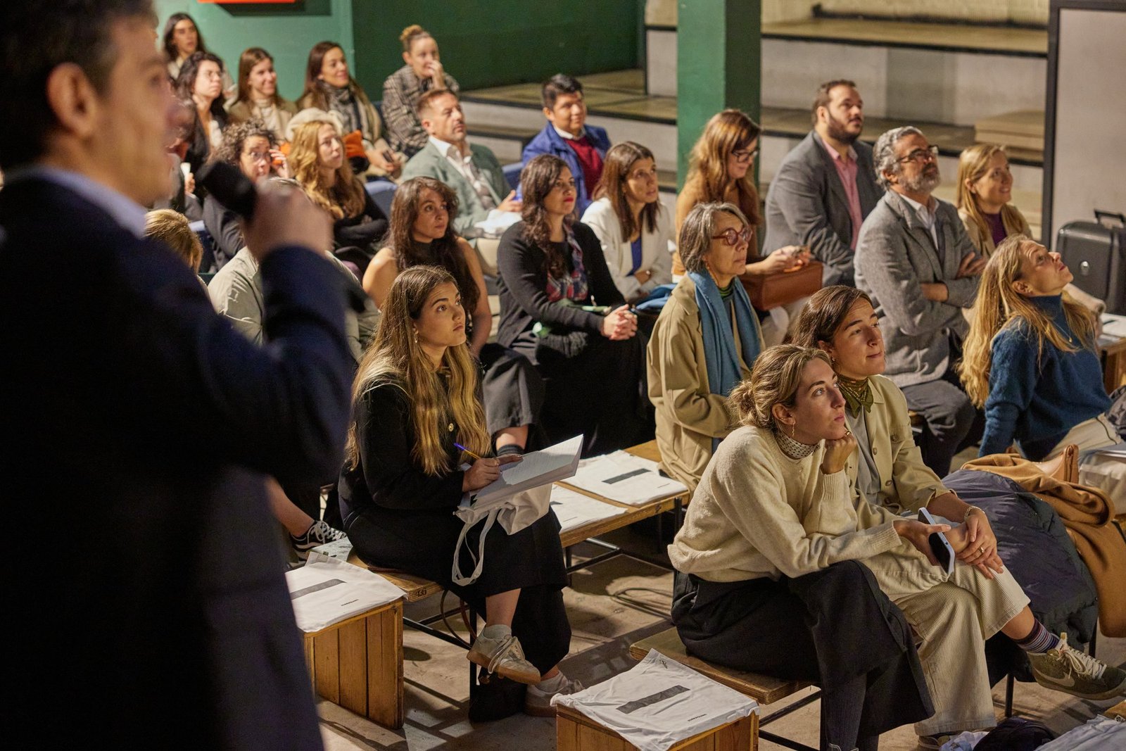 Attentive audience on tiered seating listening to a speaker with a microphone