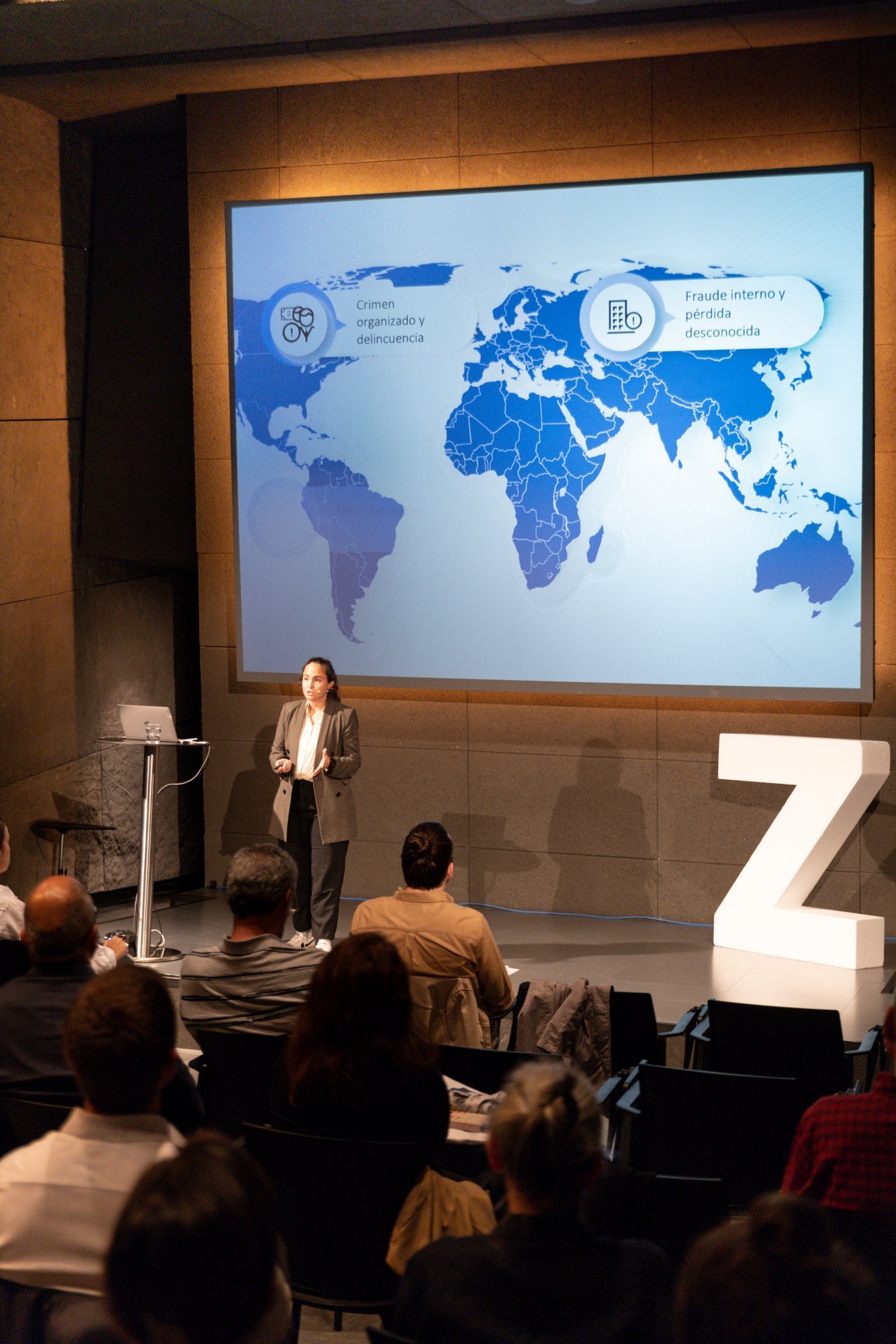 Ponente ante un mapa del mundo proyectado, junto a una gran Z, ante el público