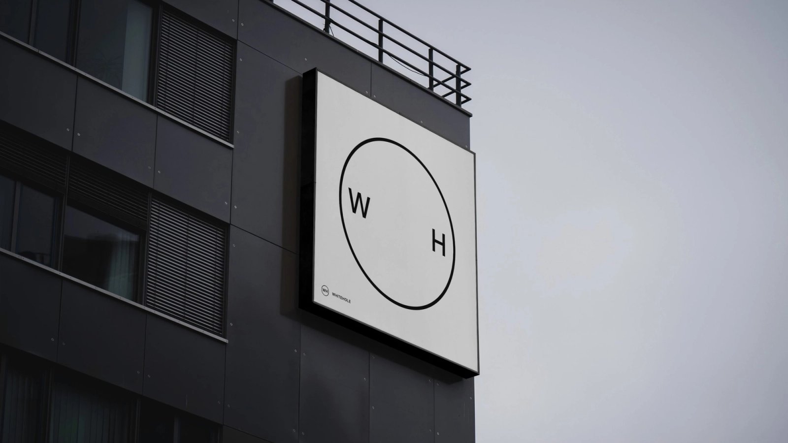 Square Whitehole sign, with the W and H inside a circle, on the dark front of a building
