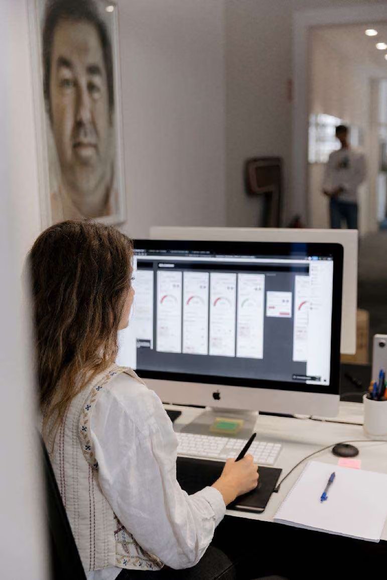 Diseñadora trabajando con tableta gráfica frente a un iMac, bajo un retrato en la pared