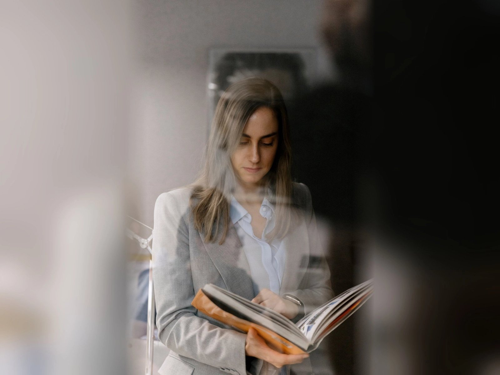 Mujer leyendo un libro de gran formato, vista a través de un cristal