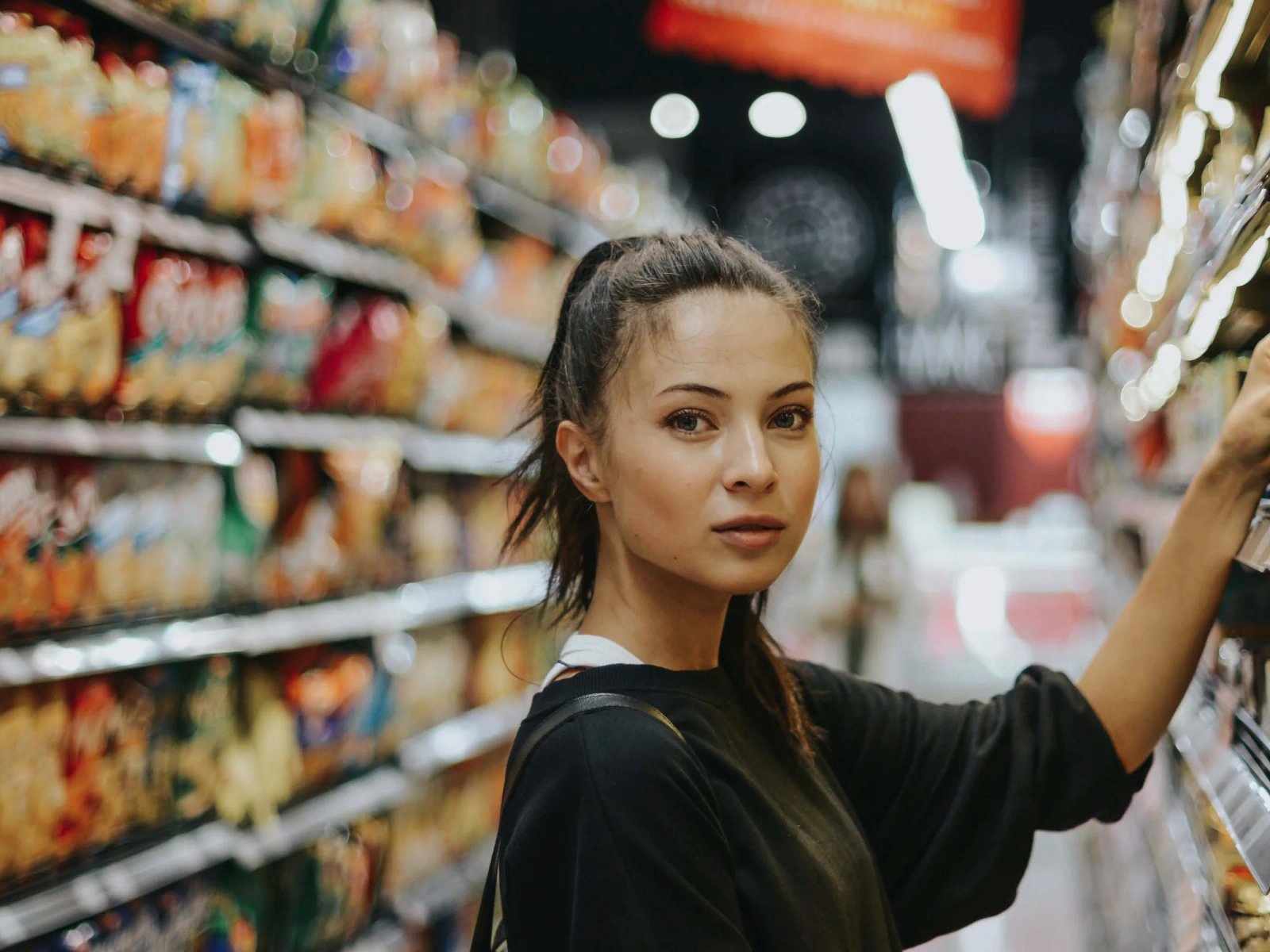 Portada de Consumer Trends 2020: una mujer mira a cámara en el pasillo de un supermercado mientras coge un producto de la estantería.