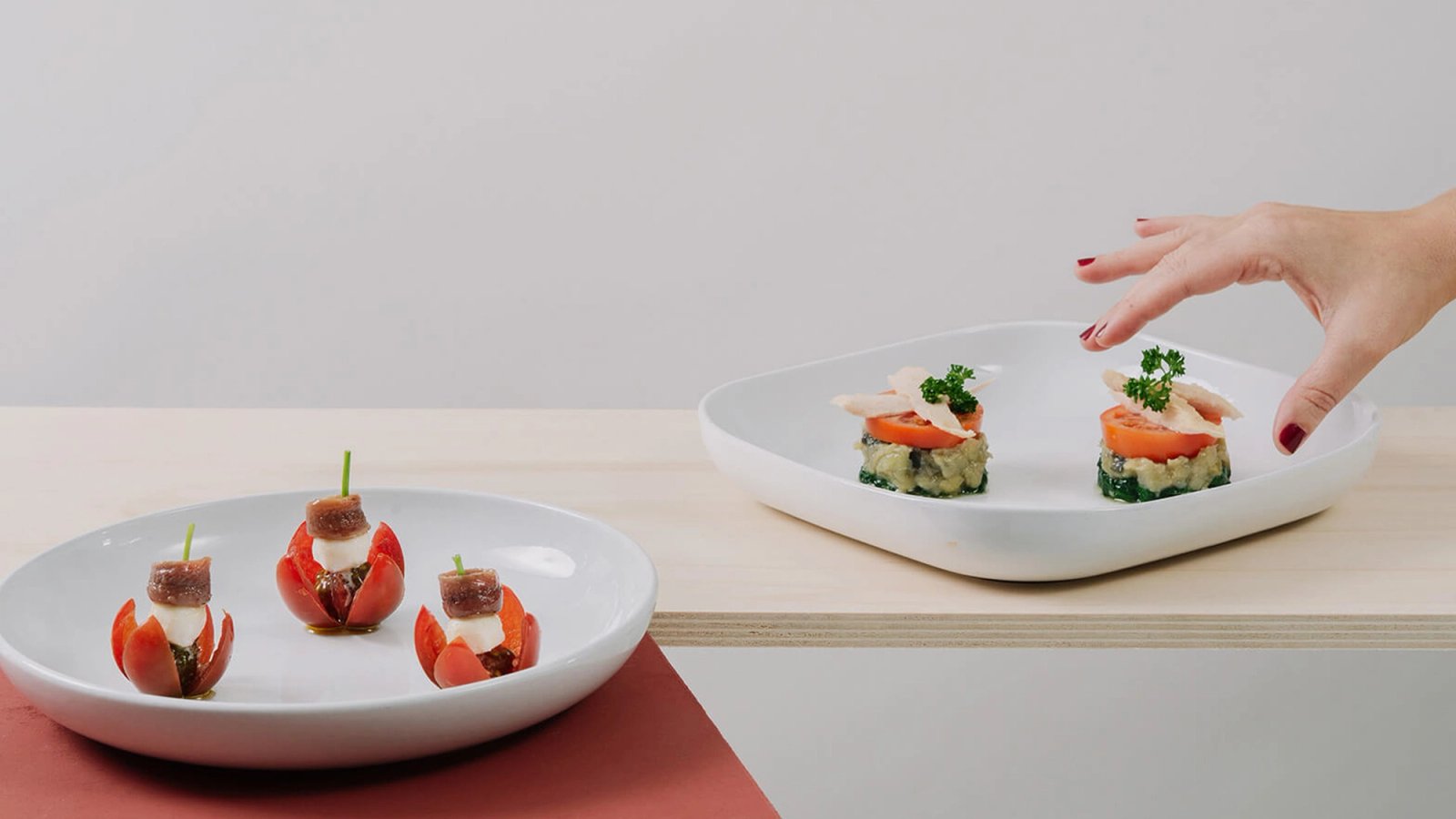 Tapas de anchoa y de bonito en platos blancos y una mano que coge una
