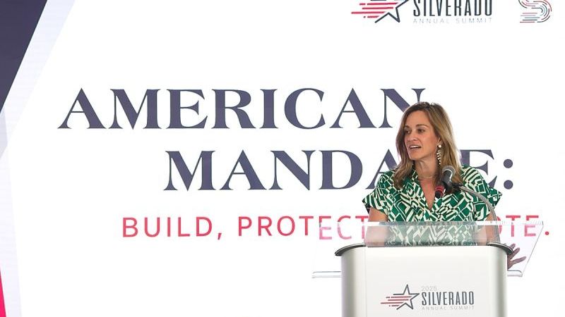 CEO Sarah Stewart Stands at a Podium in front of a backdrop that reads 2025 Silverado Annual Summit American Mandate: Build, Protect, Promote