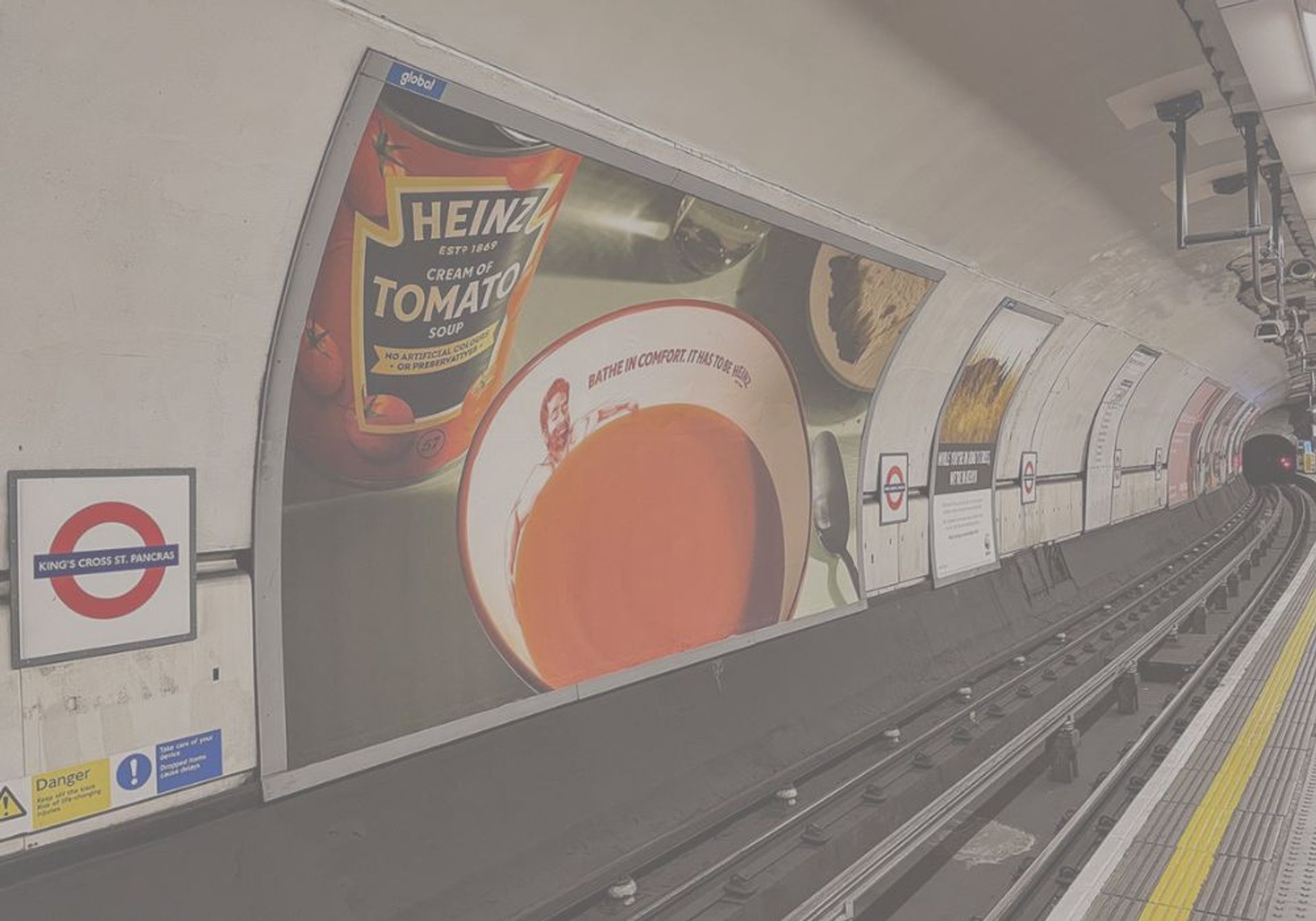 London Underground platform and tracks curving into a tunnel, with a large Heinz Cream of Tomato Soup advertisement on the wall and a "King's Cross St. Pancras" sign.