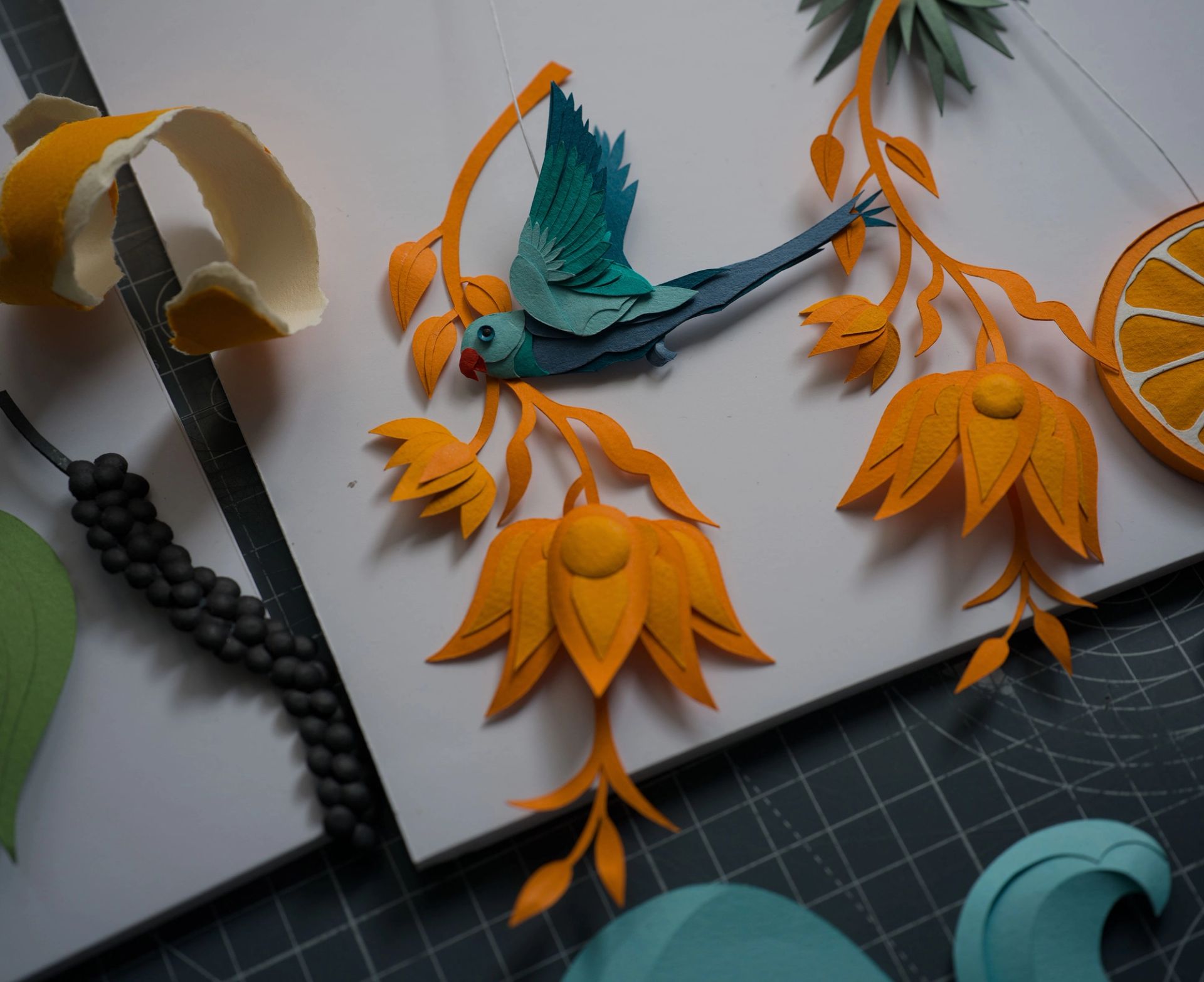 a paper bird is sitting on top of a paper flower on a cutting board .