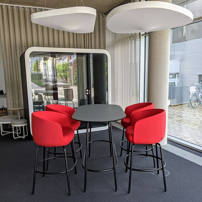 Stehtisch mit roten Barstühlen vor einer Telefonbox im Jurodo-Büro