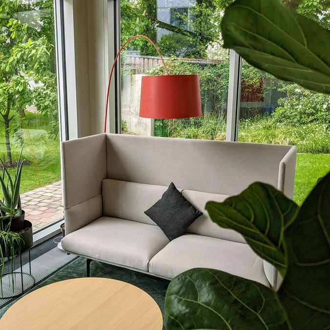 Sofa-Ecke im Jurodo-Büro mit roter Stehleuchte und Blick ins Grüne