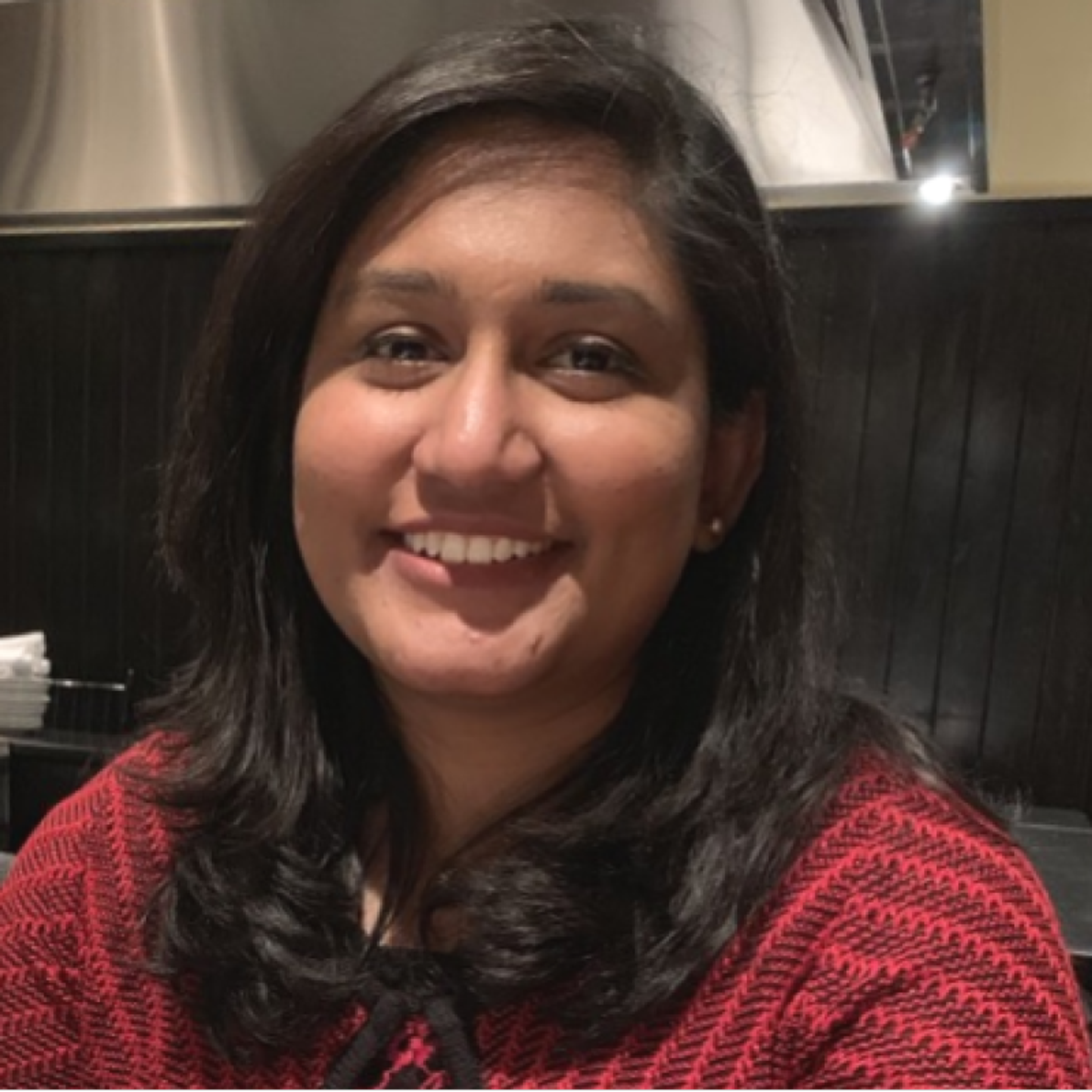 A smiling woman with dark hair wearing a red and black patterned top.