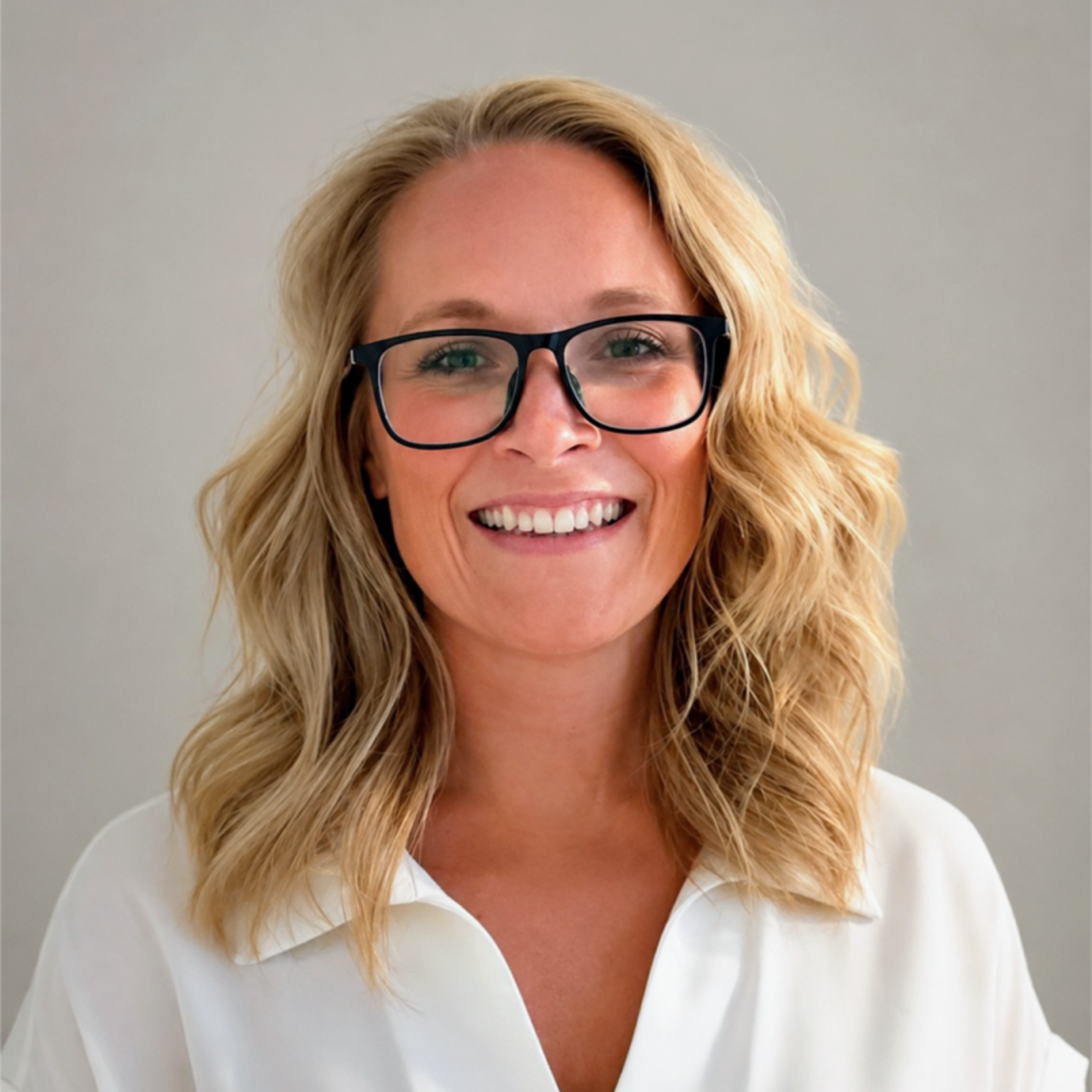 Smiling woman with blonde hair and glasses wearing a white shirt.