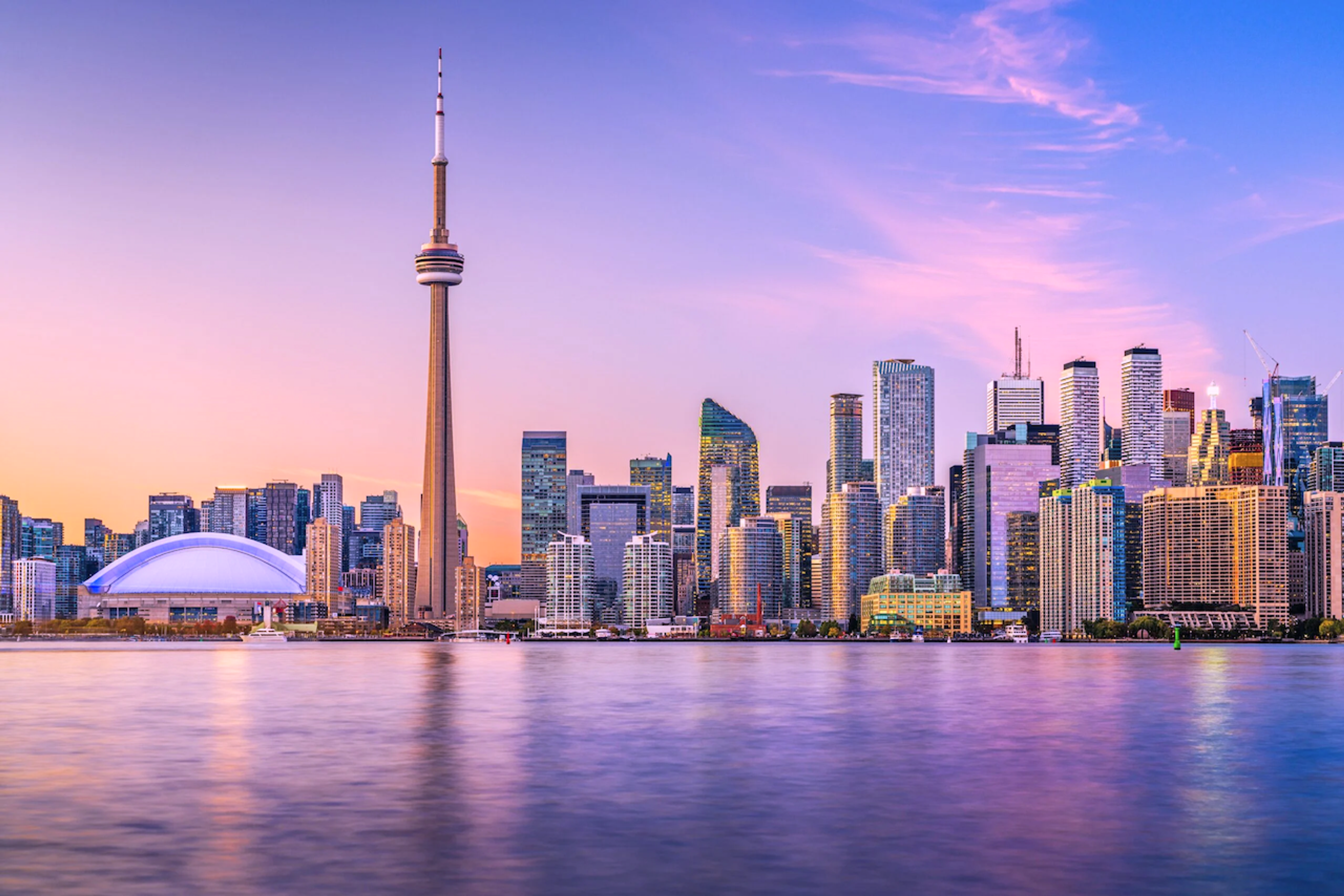 Toronto skyline with the CN Tower and Rogers Centre at sunset, reflected in the water.