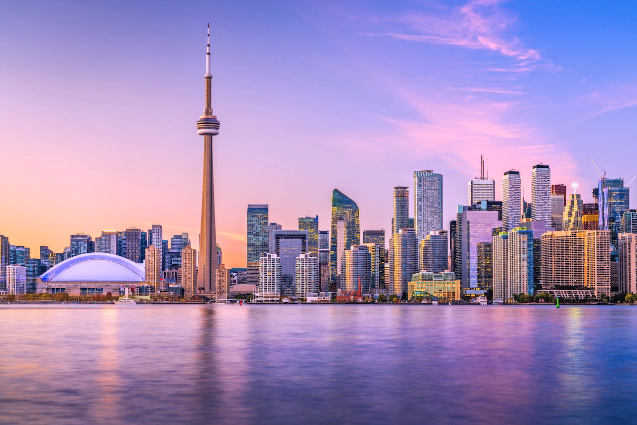 Toronto skyline with the CN Tower and Rogers Centre at sunset, reflected in the water.
