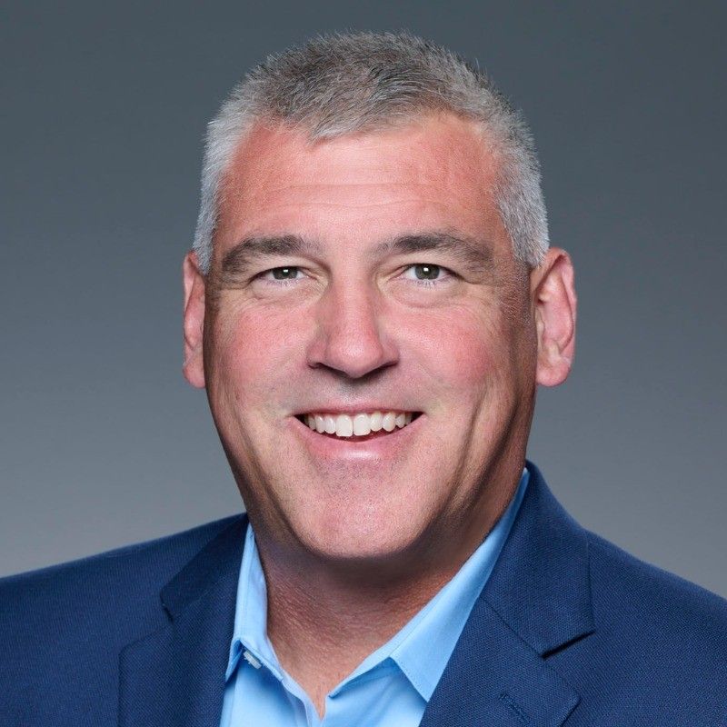 Headshot of a smiling man with gray hair in a blue suit jacket.