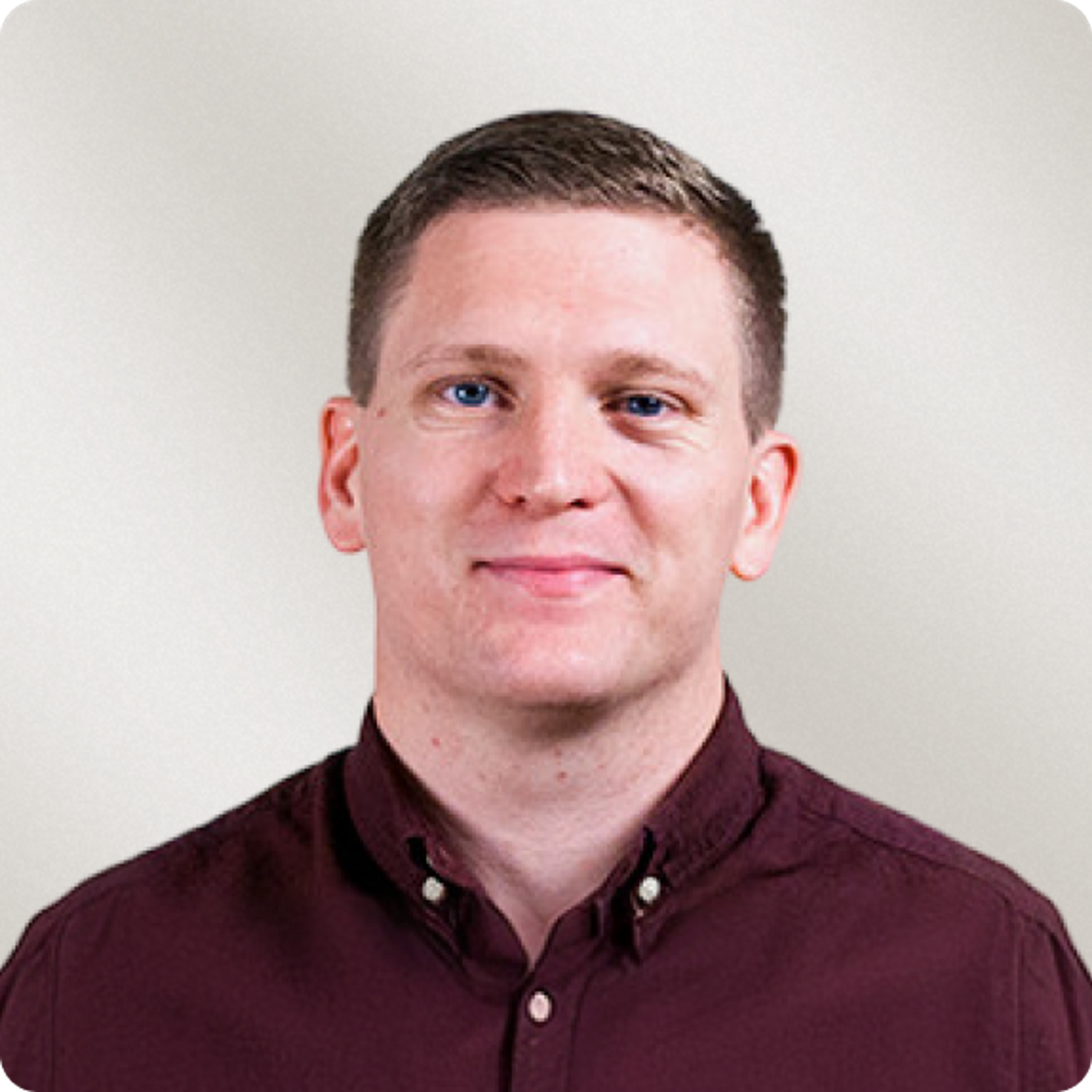 A smiling man with short dark hair and a maroon shirt.