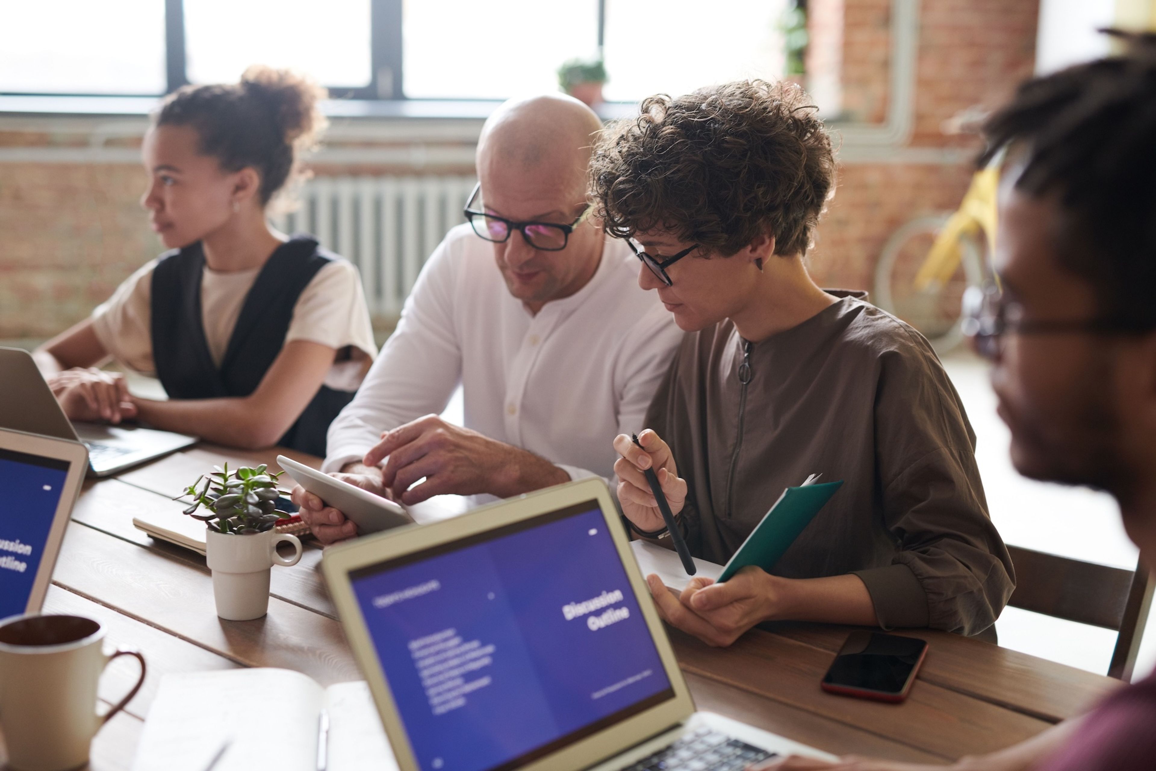 Four diverse people working at a table with laptops and tablets.