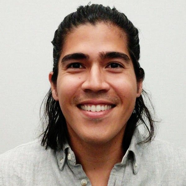 A man with long dark hair pulled back, smiling and wearing a grey collared shirt.