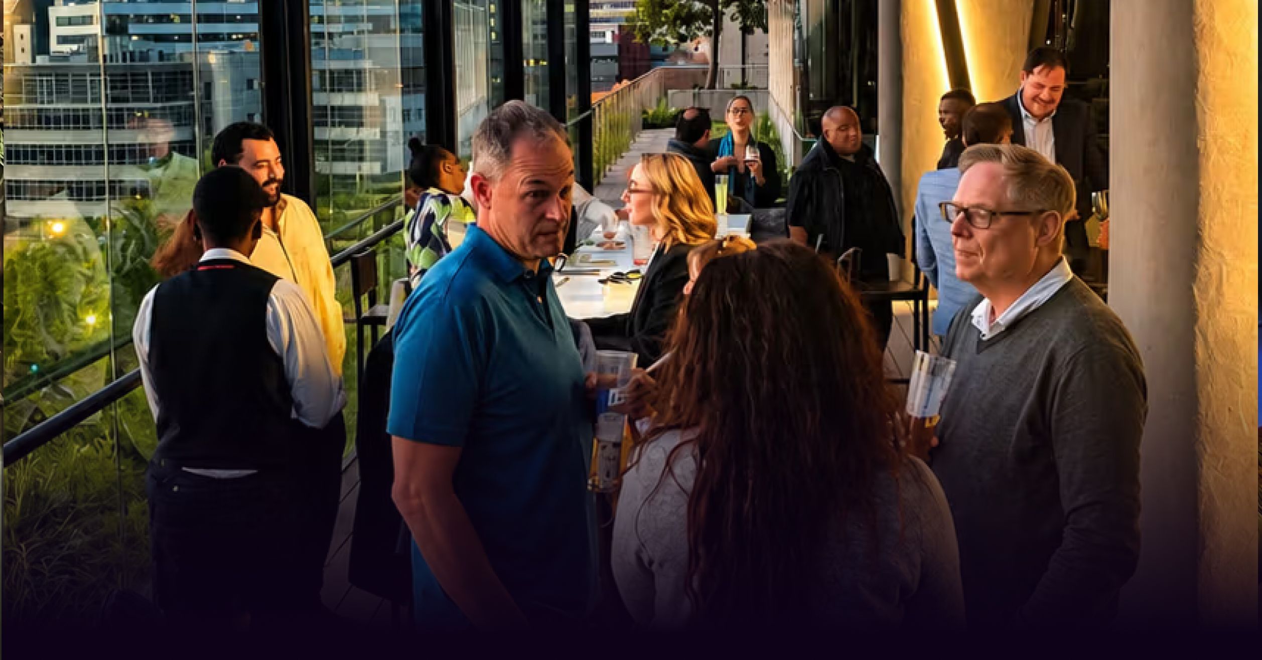 People socialize on a modern rooftop patio overlooking a cityscape.