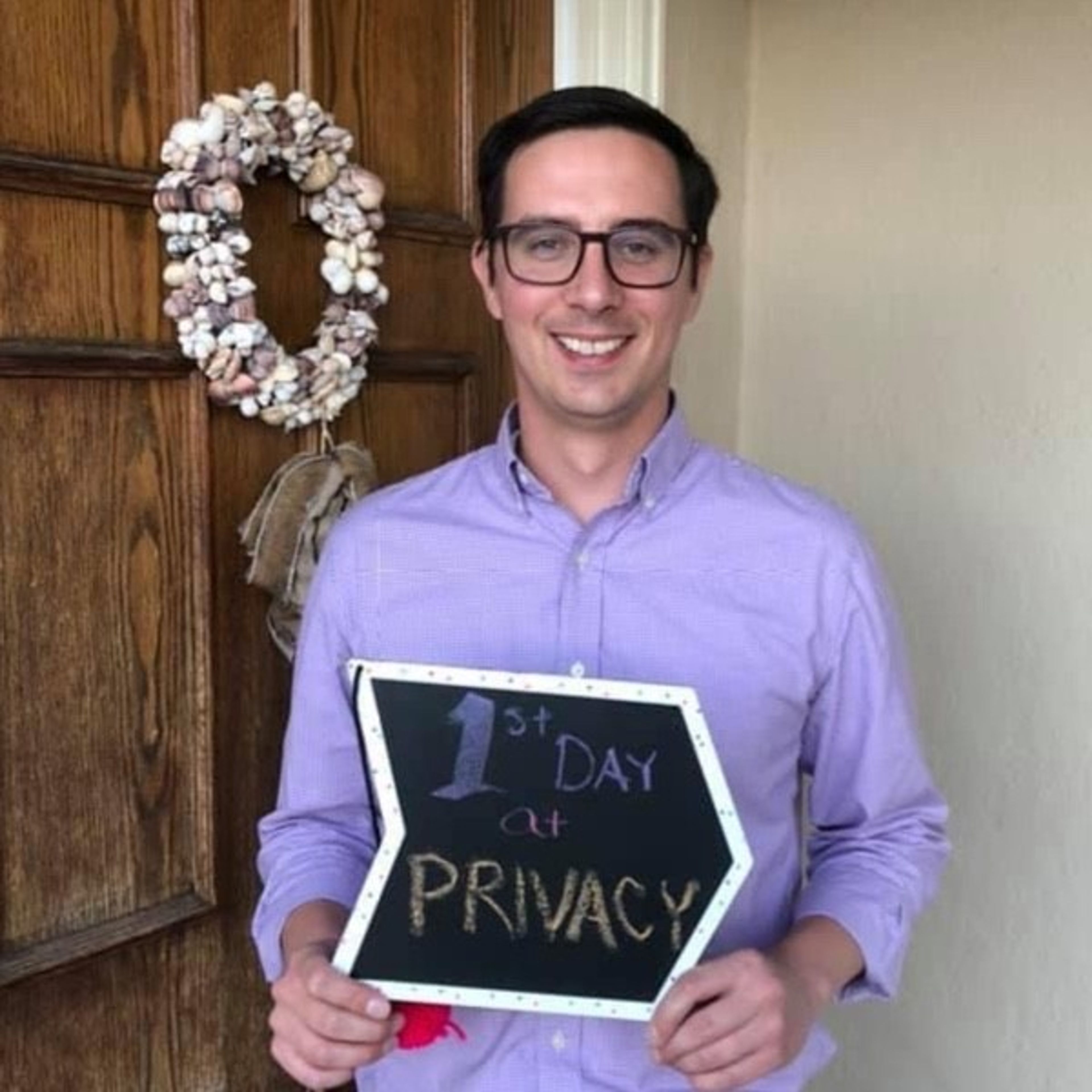 A smiling man in a purple shirt holds an arrow-shaped sign that reads "1st DAY at PRIVACY."