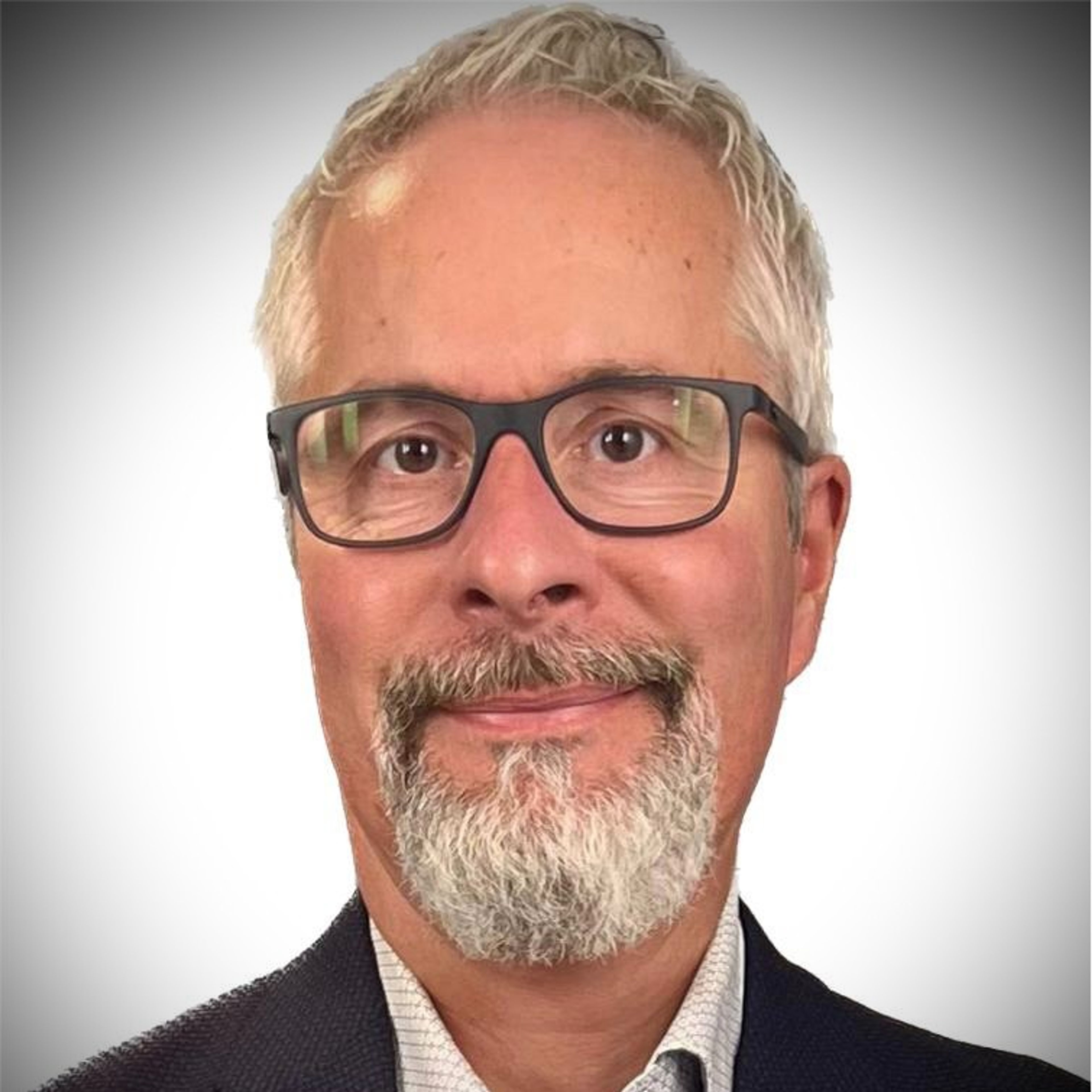 Headshot of a smiling man with gray hair, a gray beard, and black-rimmed glasses, wearing a dark blazer.