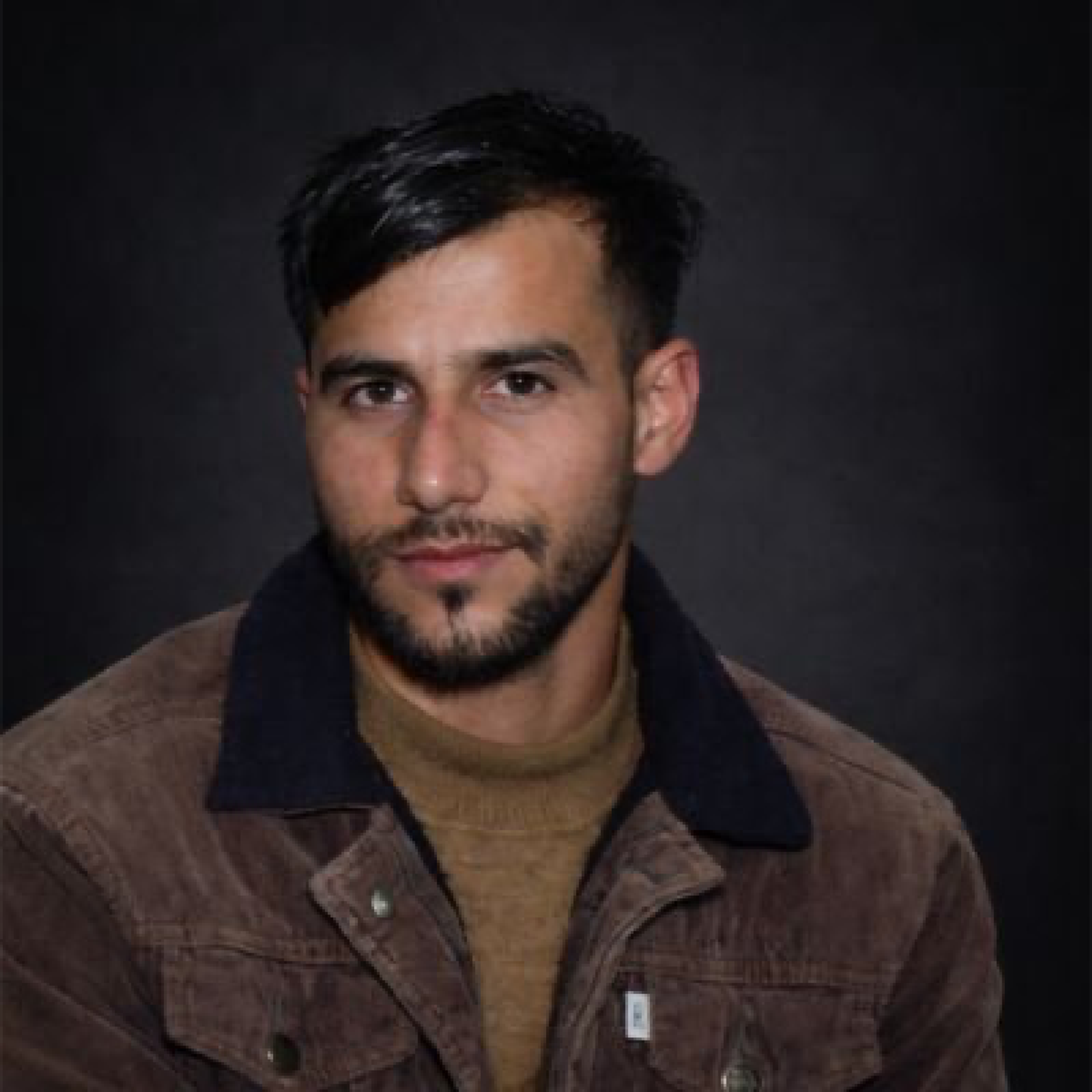 Man with dark hair and beard wearing a brown corduroy jacket.
