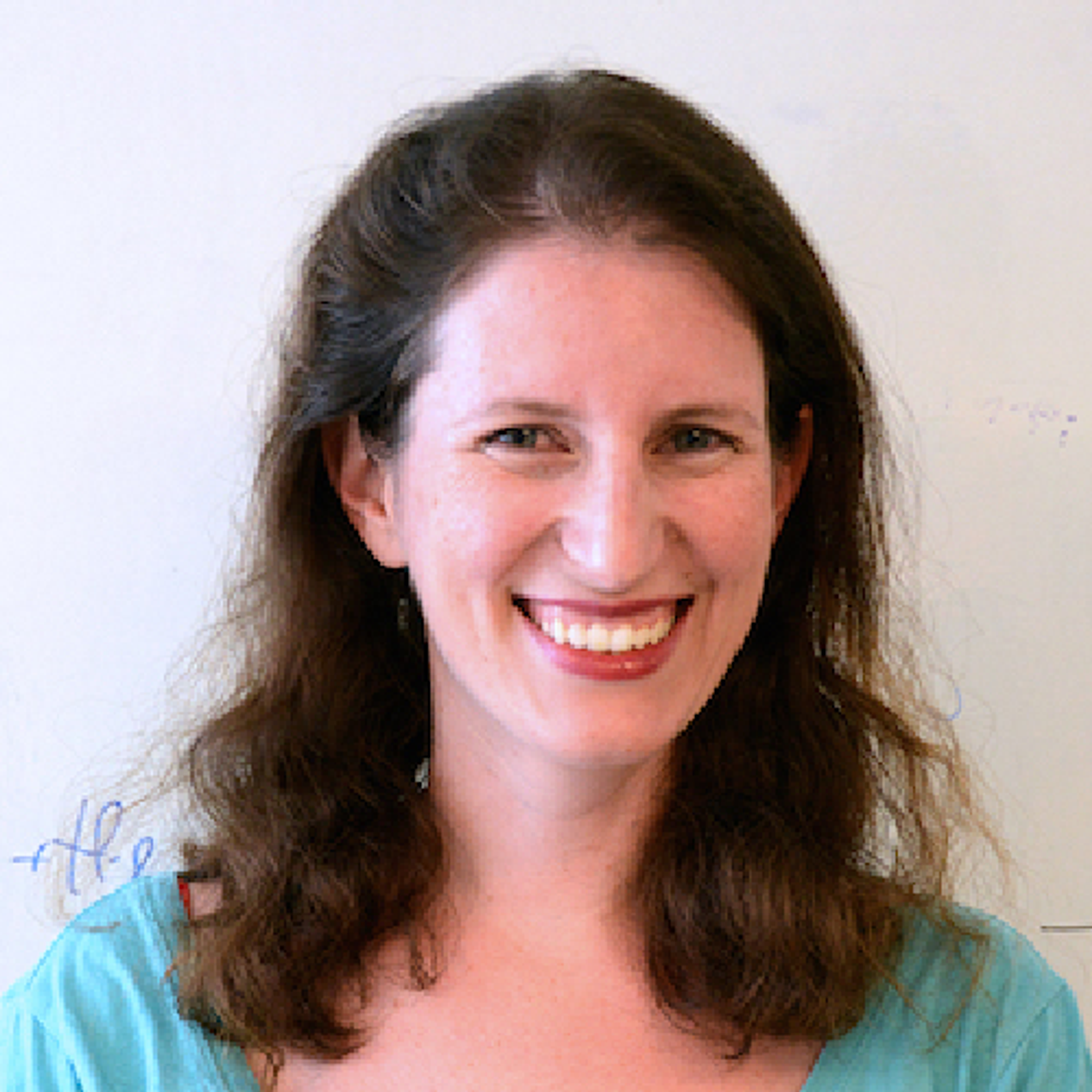 A smiling woman with long brown hair wears a blue-green top.
