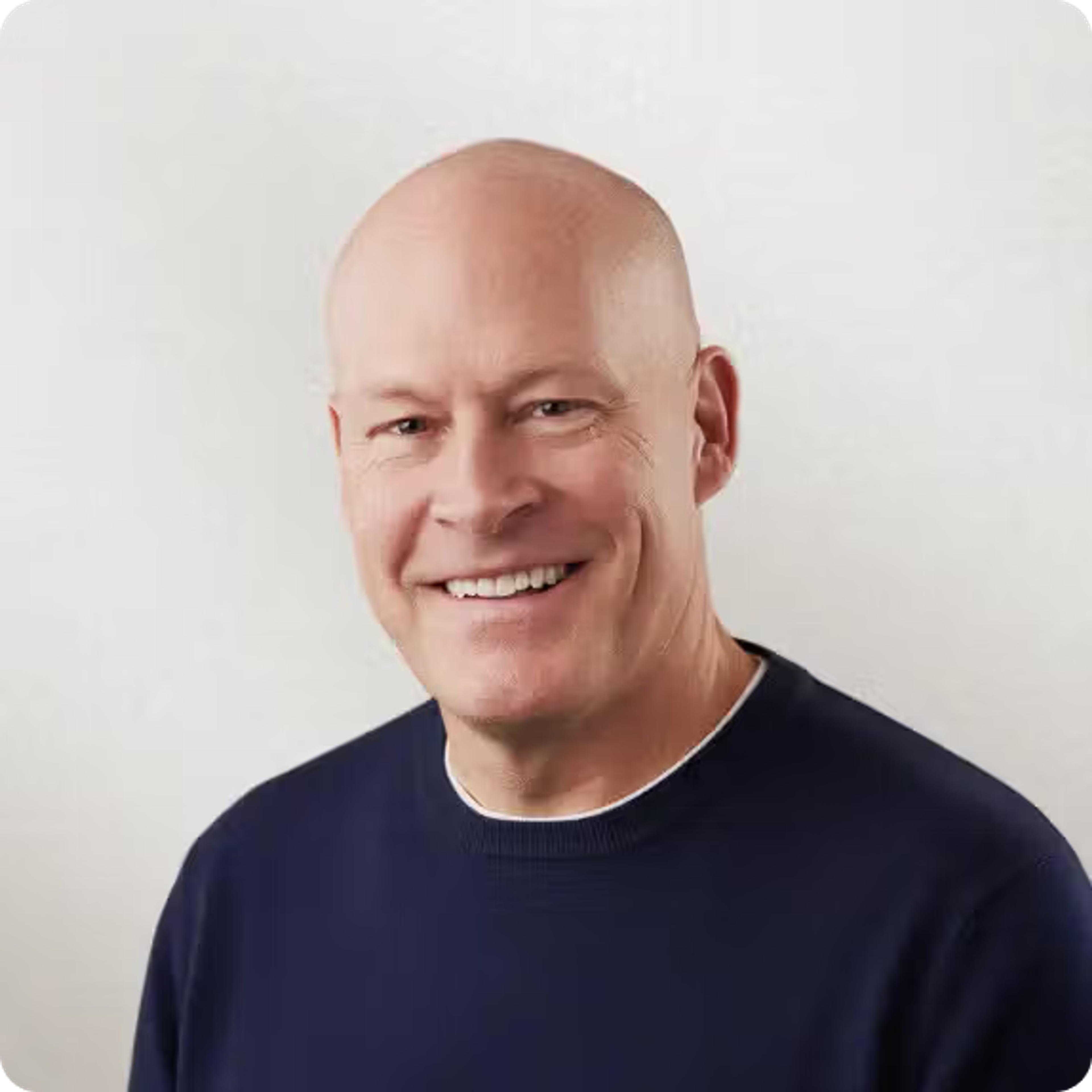 A smiling bald man in a navy blue sweater.
