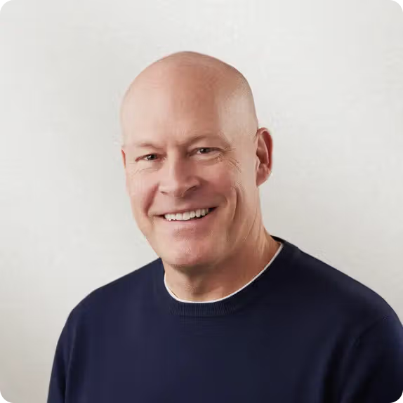 A smiling bald man in a navy blue sweater.