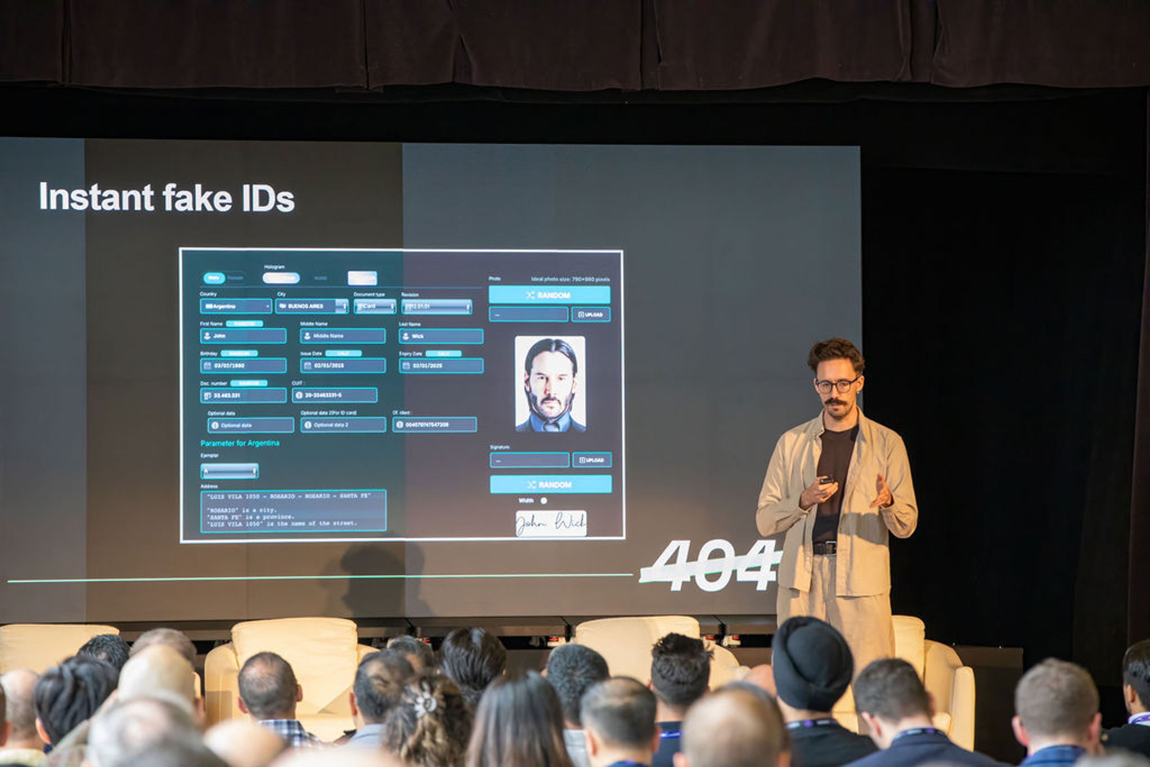 A presenter on stage stands next to a screen displaying an "Instant fake IDs" interface with a photo of Keanu Reeves.
