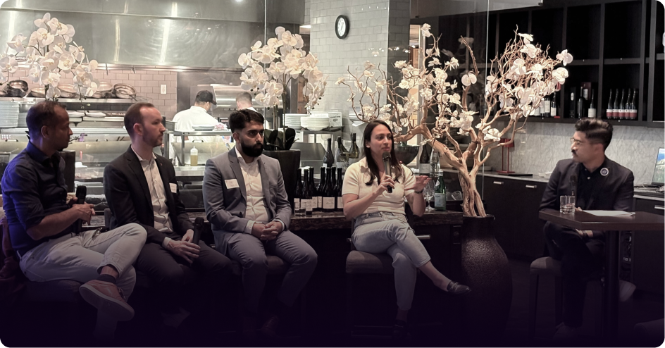 A diverse panel of five people (four men, one woman) seated at a restaurant, with the woman speaking into a microphone.