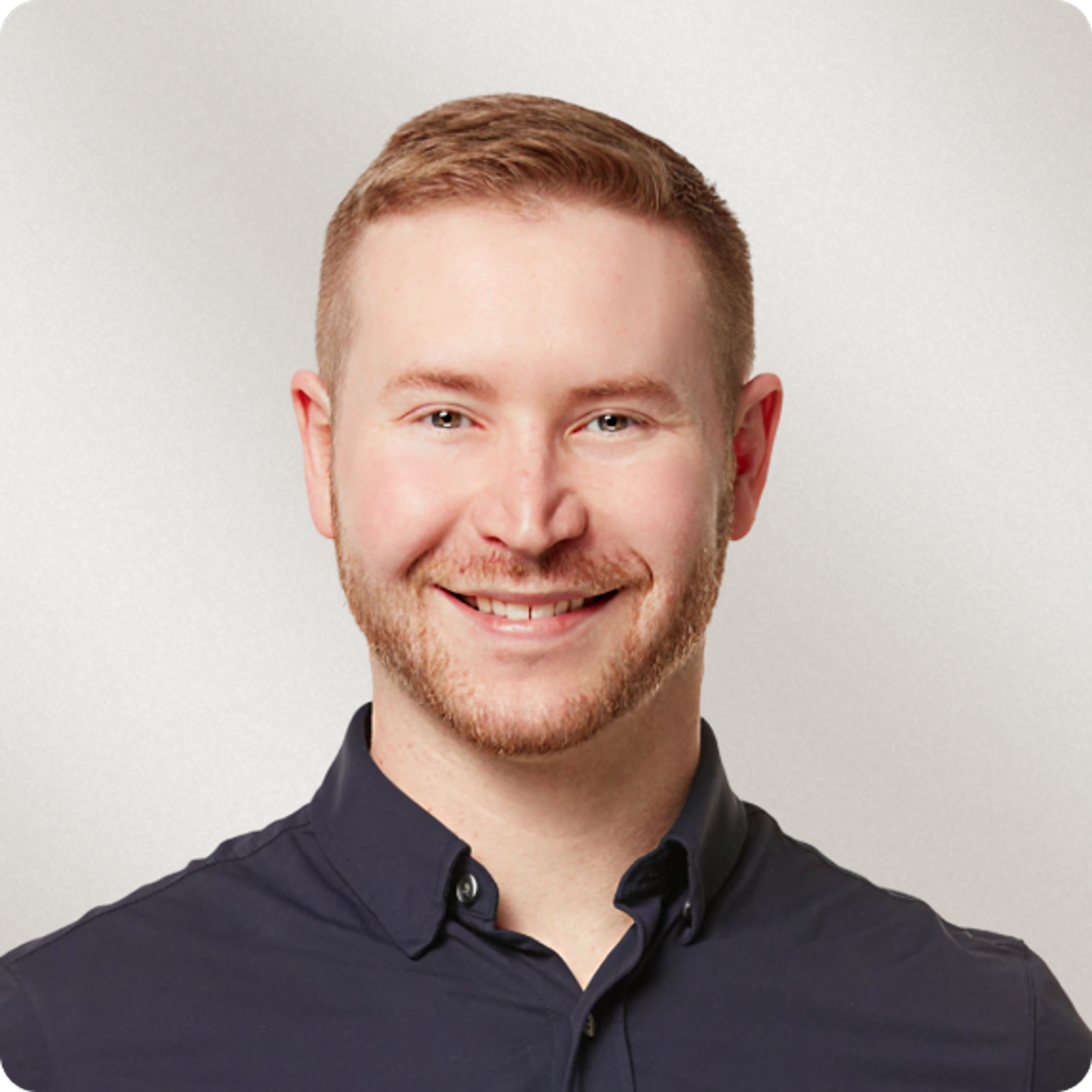 Headshot of a smiling man with a short beard and brown hair, wearing a dark blue shirt.