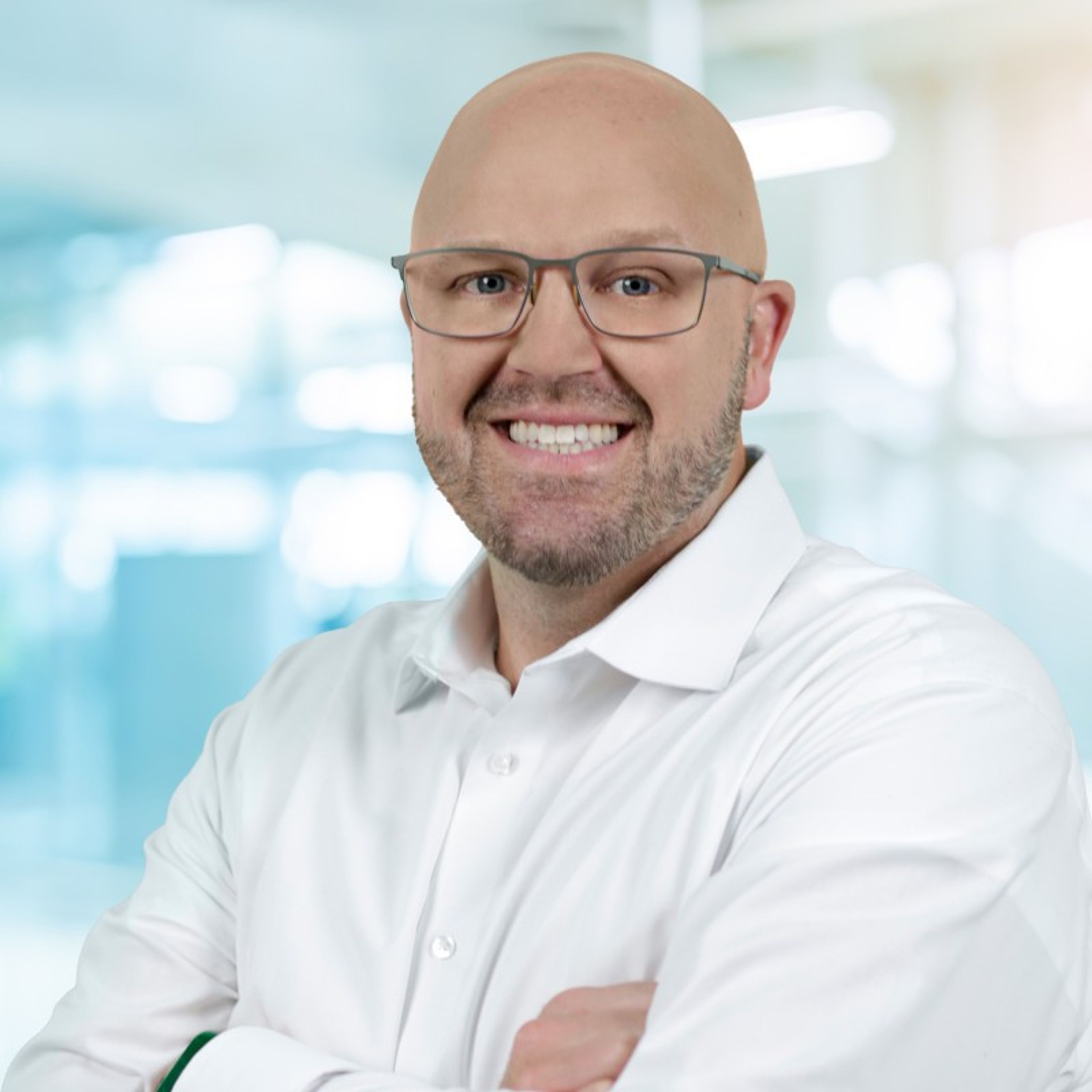 Smiling bald man with a beard and glasses, wearing a white shirt with arms crossed.