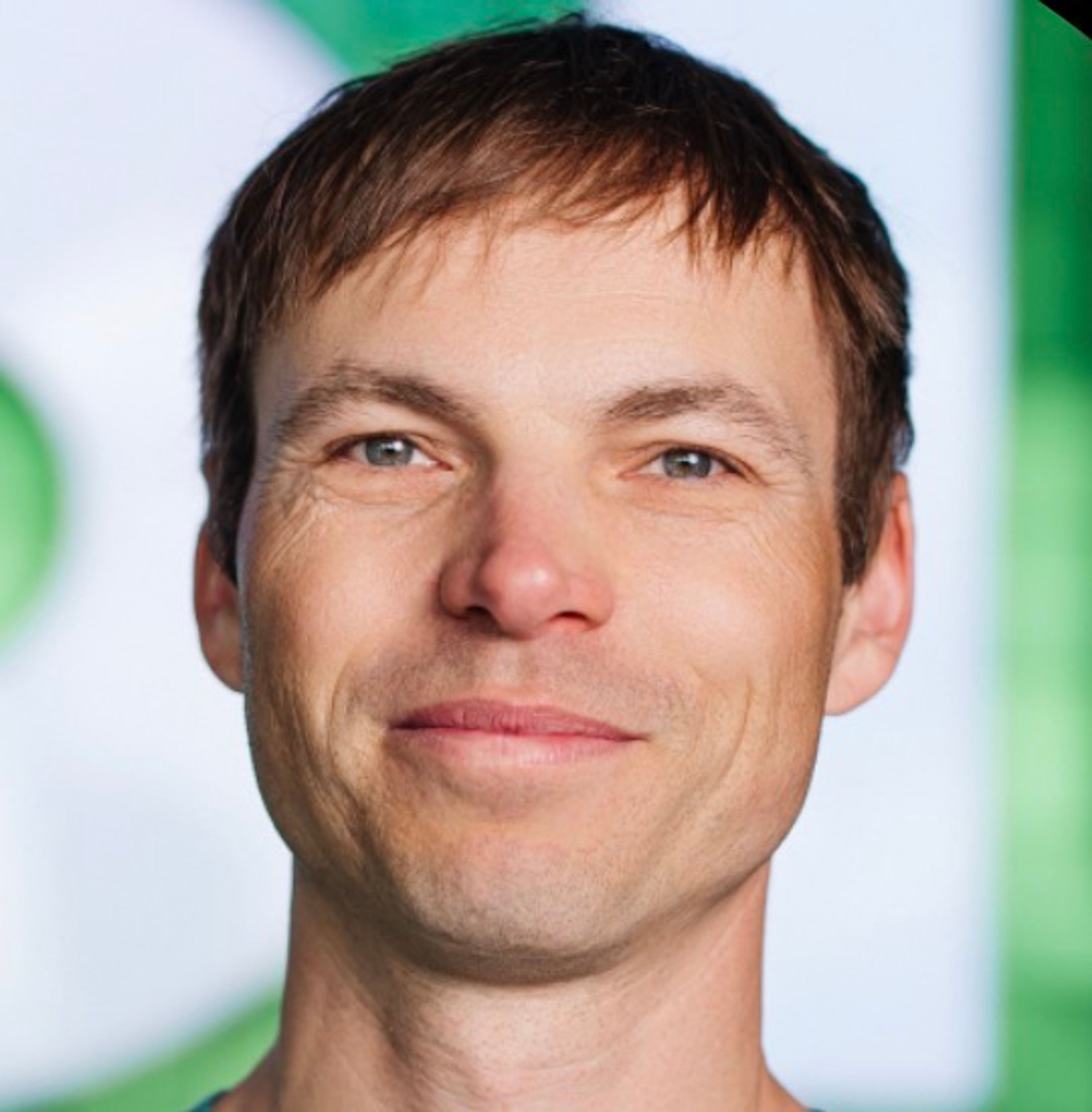 Close-up of a man with short brown hair and blue eyes smiling slightly.