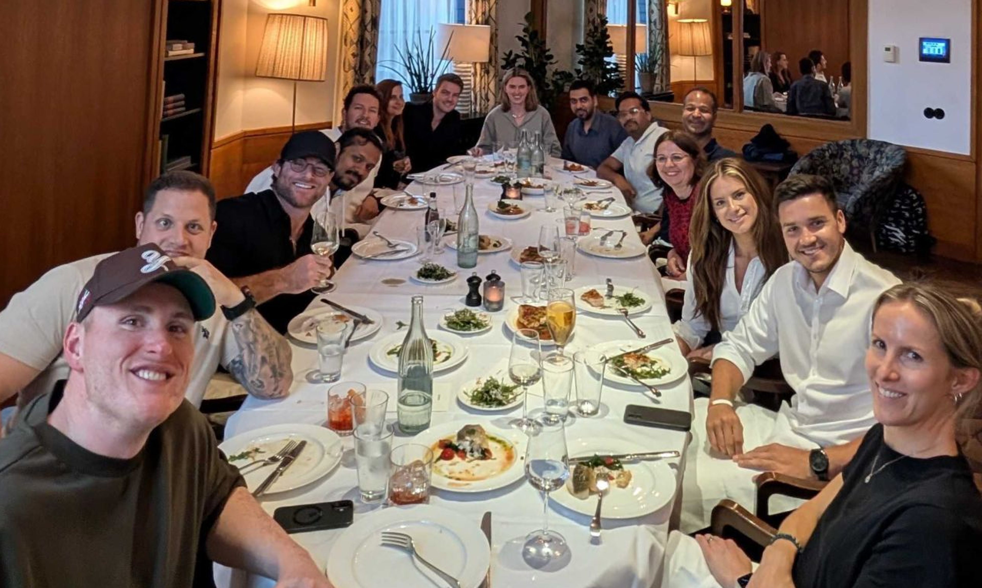 A group of smiling people dining together at a long table in a restaurant.