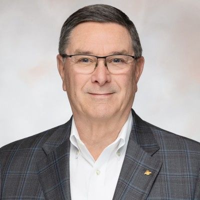 Smiling man with grey hair and glasses wearing a plaid suit jacket.