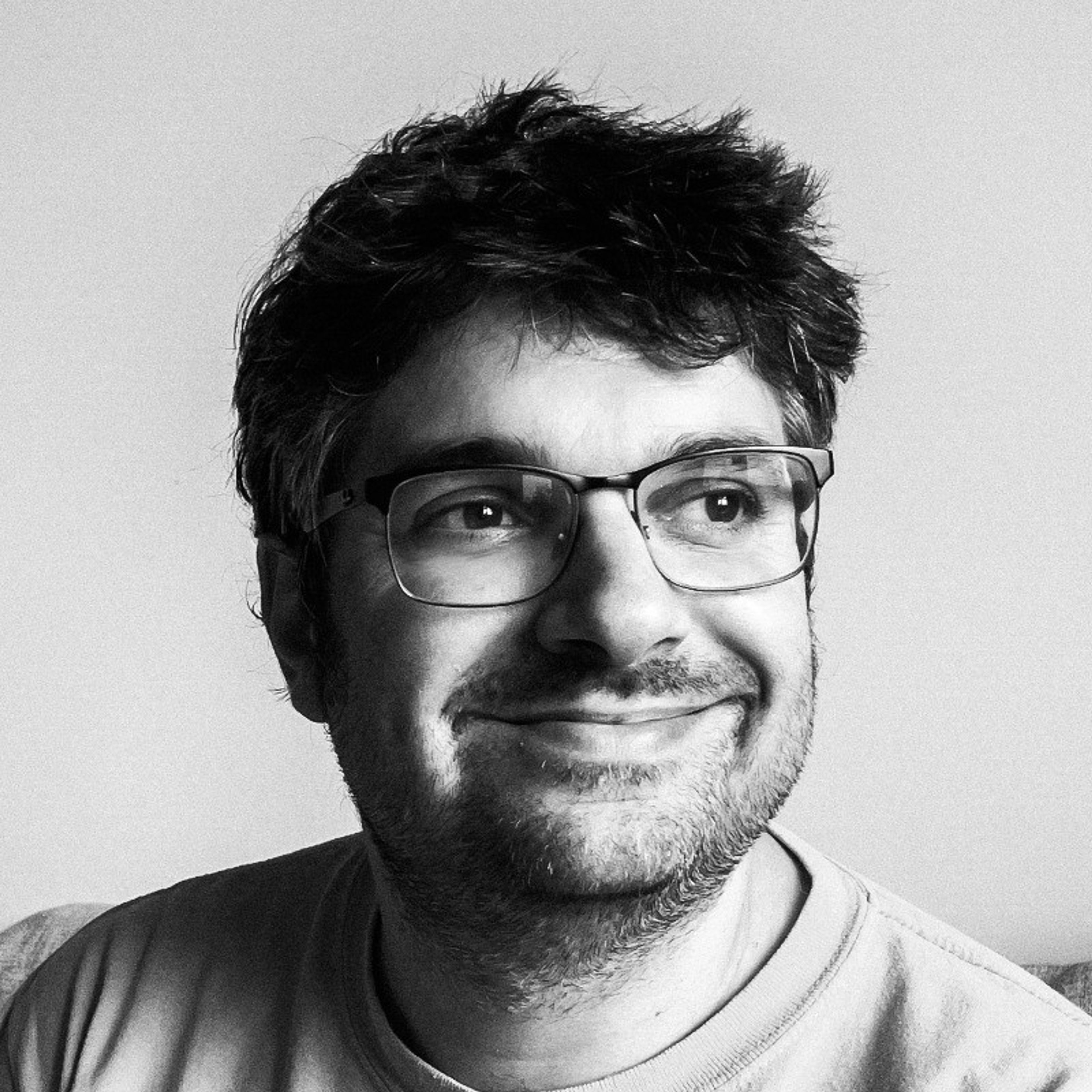 Black and white close-up of a smiling man with glasses and messy hair, looking to the right.