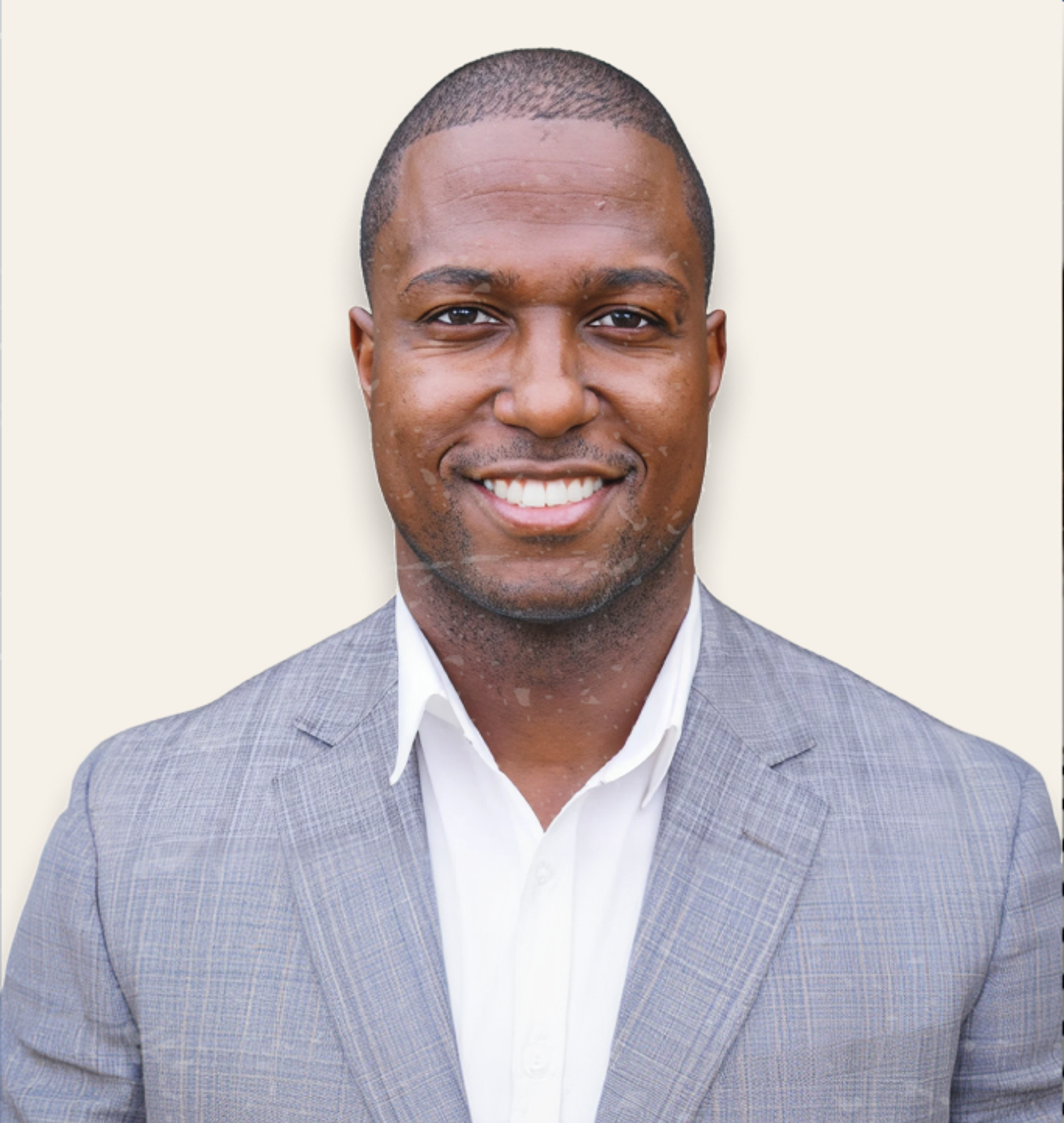 A smiling Black man in a grey suit jacket and white shirt.
